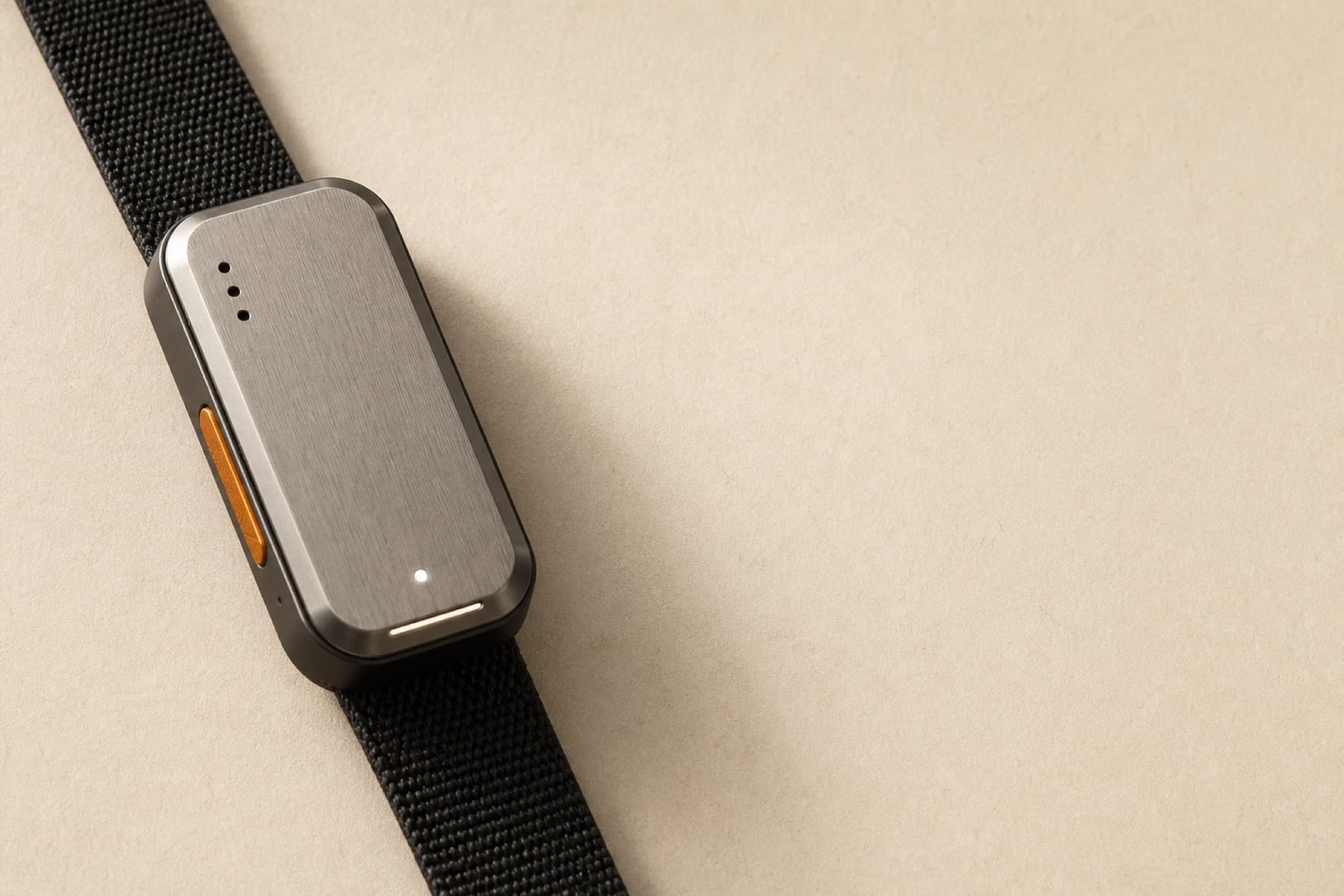LARS/01, a small charcoal slab with a brushed steel face and one burnt orange button on its edge, on a black woven strap